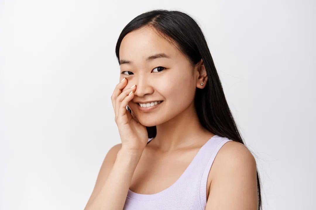 Perempuan Asia tersenyum menunjukkan kulit wajah sehat dan terhidrasi setelah menggunakan moisturizer untuk kulit berminyak.