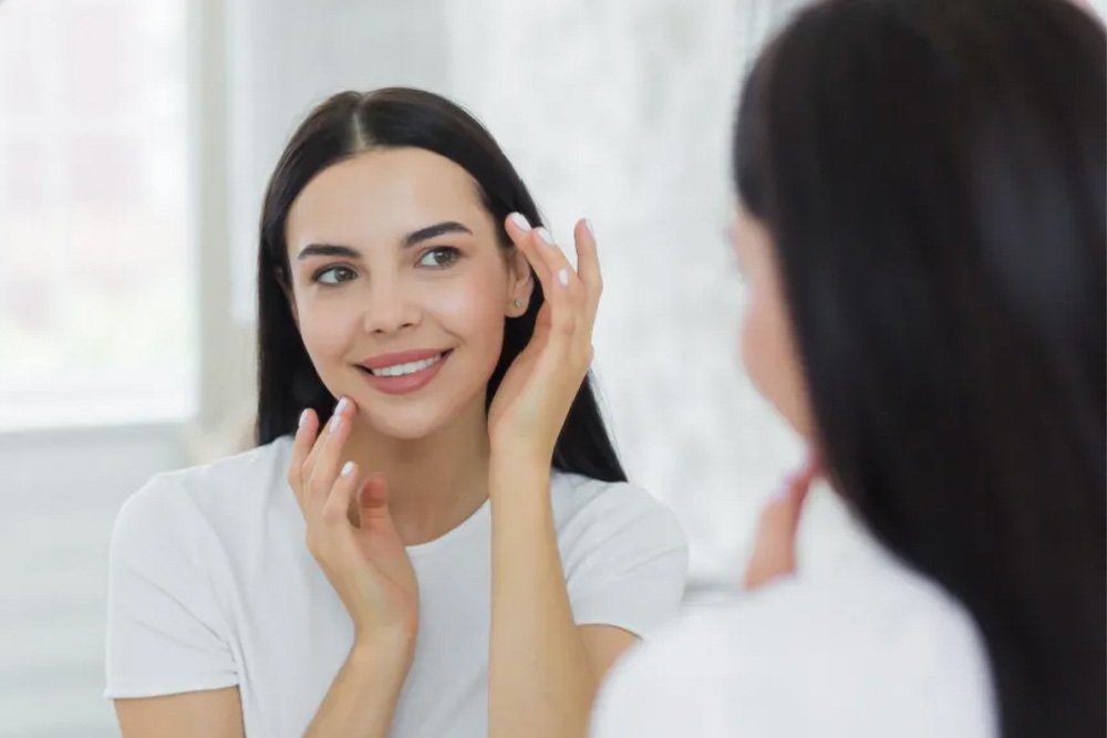 wanita di depan kaca sedang menggunakan tri acid peeling serum